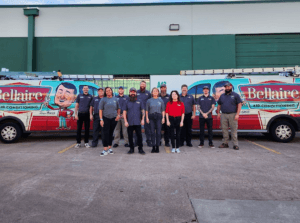 A large group of employees wearing smiles, gathered proudly in front of branded Bellaire Air Conditioning HVAC vans, showcasing unity and dedication to their company's mission.